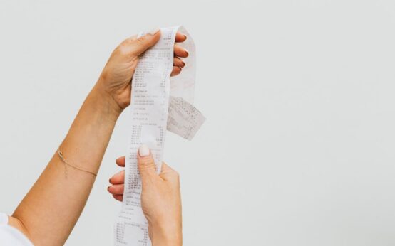 A detailed view of a person holding a long shopping receipt against a plain background.