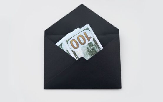 Hundred dollar bills partially visible in an open black envelope on a white background.